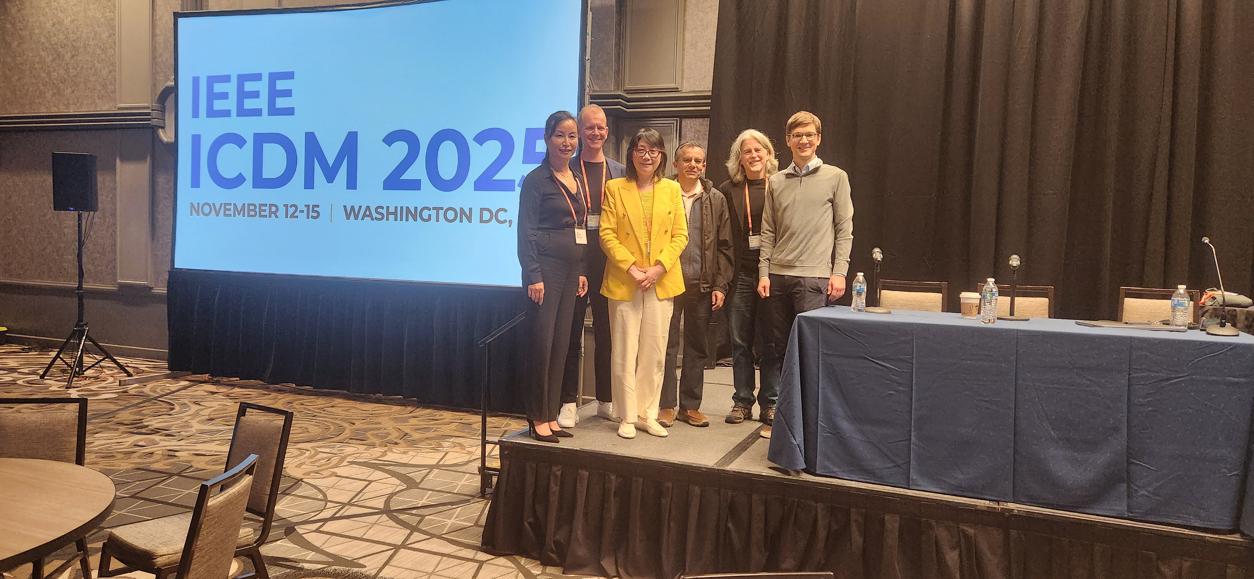 ICDM 2025 panelists posing in front of the conference screen.
