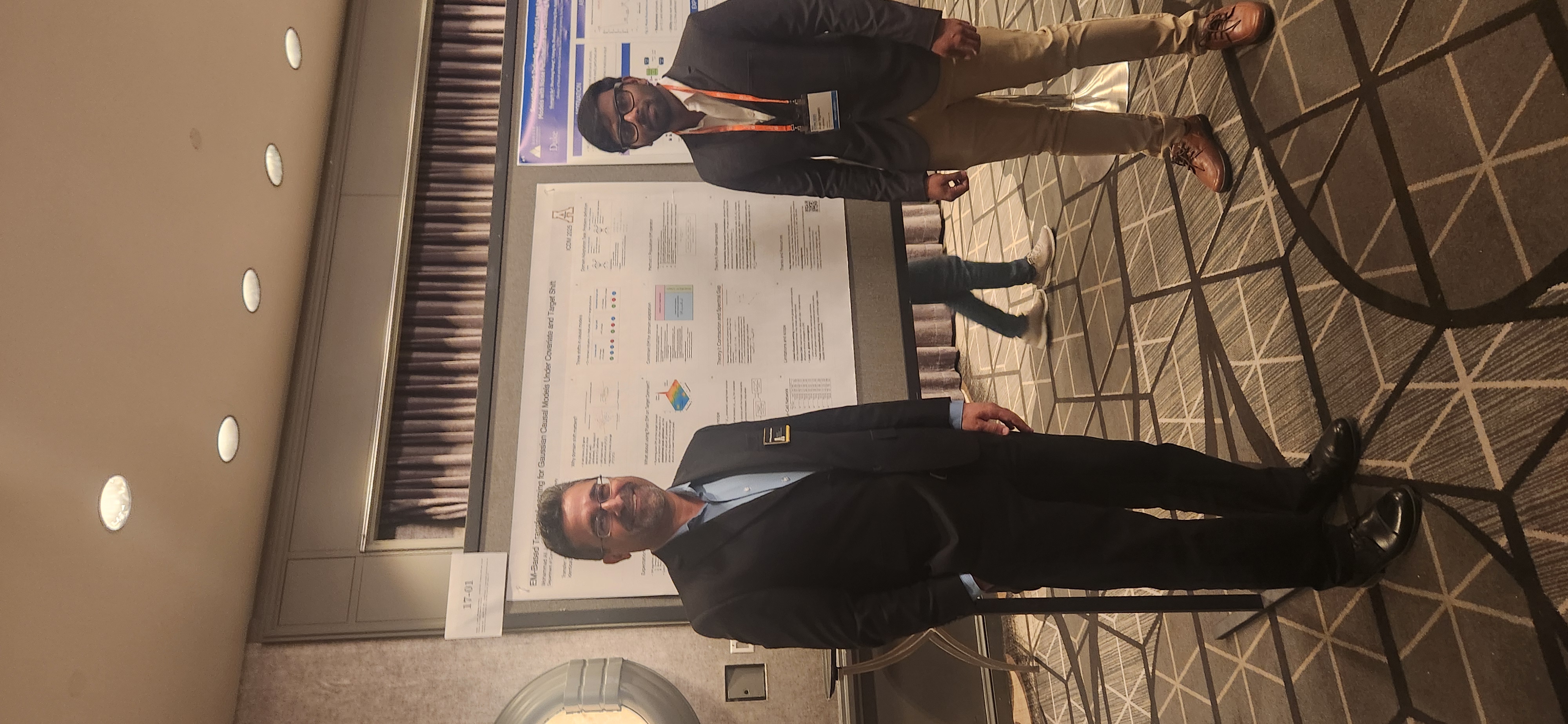 Presenter and a colleague standing next to the EM-based transfer learning poster.
